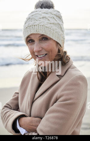 L'Espagne, Minorque, portrait of smiling senior woman wearing bobble hat sur la plage en hiver Banque D'Images