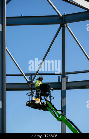 Cadre d'acier du nouveau bâtiment en construction à l'ouvrier de la construction sur l'inspection levage grue ensemble conjoint contre le ciel bleu. Banque D'Images