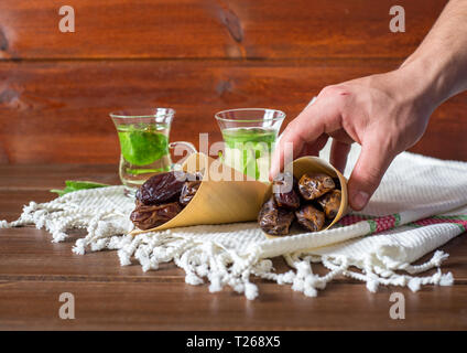 L'Iftar ou Suhoor snack , main d'un homme avec un conus de dates avec mentha plateau sur fond , Ramadan concept Banque D'Images