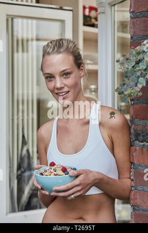 Portrait of smiling sporty woman avec bol à muesli house entrée Banque D'Images