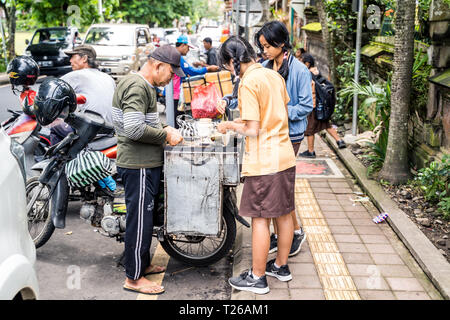 Ubud, Bali, Indonésie - Janvier 2019 : les filles en uniforme d'acheter de la nourriture à un vendeur de rue pendant la pause de midi Banque D'Images