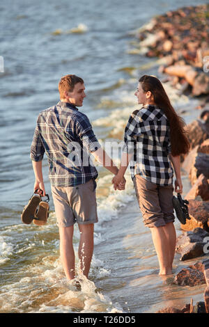 Jeune couple en chemises à carreaux à marcher le long de la rive du lac au coucher du soleil Banque D'Images