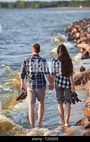 Jeune couple en chemises à carreaux à marcher le long de la rive du lac au coucher du soleil Banque D'Images