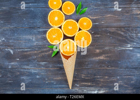 Plat à l'obscurité créative jeter Vue de dessus des tranches de fruits d'orange dans la crème glacée cornet gaufré sur fond de table en bois brun avec copie espace. Un minimum de Banque D'Images