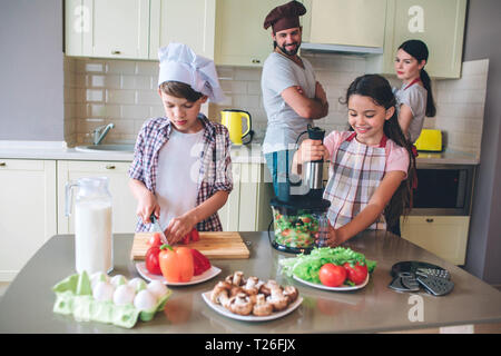 Les enfants sont indépendants preparing salad ensemble sans les parents. Le mélange est fille de légumes dans blender alors que boy est le découpage en morceaux de tomates. Parents l Banque D'Images