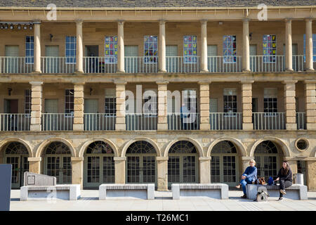 Les femmes assises sur un banc en face du mur est colonnades colonnade / / balcon / balcons de la Pièce Hall. Graines de soleil et ciel bleu. Halifax, West Yorkshire, Royaume-Uni. (106) Banque D'Images