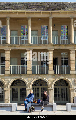 Les femmes assises sur un banc en face du mur est colonnades colonnade / / balcon / balcons de la Pièce Hall. Graines de soleil et ciel bleu. Halifax, West Yorkshire, Royaume-Uni. (106) Banque D'Images