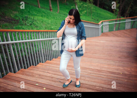 La grossesse, la maternité, les gens et l'attente concept - close up of pregnant woman with shopping bags au parc. Banque D'Images