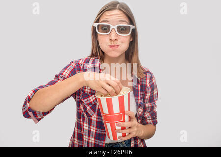 Jeune femme dans les verres debout et regardant tout droit. Elle mange du pop-corn et a fort dans les mains. Elle a soufflé les poussins. Modèle est satisfait. Isolé sur g Banque D'Images