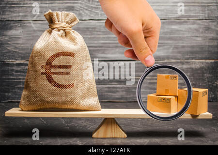 Loupe est à la recherche d'un sac d'argent euro et un tas de boîtes sur les échelles. Les relations économiques entre les sujets, le modèle économique mondial. Banque D'Images