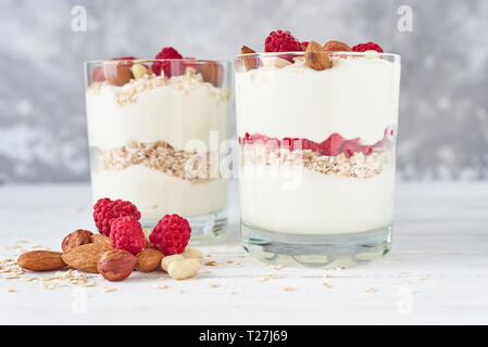 Deux verres de granola yogourt grec avec des framboises, des flocons d'avoine et les noix sur fond blanc. La nutrition saine Banque D'Images