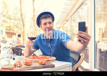 En prenant l'homme Hipster avec selfies grande pizza bruschetta et en maintenant le verre de vin rouge Banque D'Images