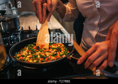 Couper vue de l'homme tenant la main sur la femme. Ils faire cuire le dîner ensemble. Couple friture sur pan Banque D'Images