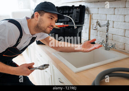 Handyman vérifier pour des fuites. Il tenir la main sous elle. Homme debout dans la cuisine à l'évier. La boîte à outils et flexible sur 24 Banque D'Images