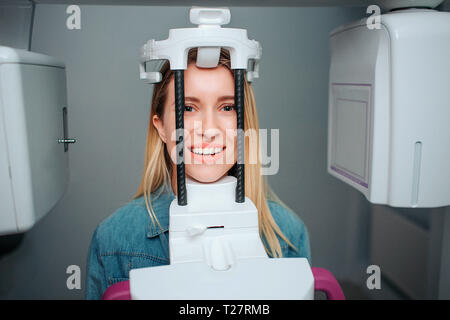 Heureux jeune femme positive s'asseoir dans la salle du dentiste. Elle a top hat pour faire x-ray dents procédure. Femmes plus sur la caméra et sourire. Banque D'Images