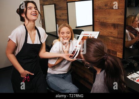 Coiffeur professionnel et blonde jeune femme en riant tout en choisissant la couleur de cheveux de palette en instituts de beauté Banque D'Images