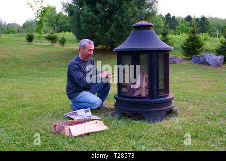 Un homme de race blanche, 50 ans, est sur le point d'allumer sa cheminée en plein air le soir, dans son arrière-cour. Banque D'Images