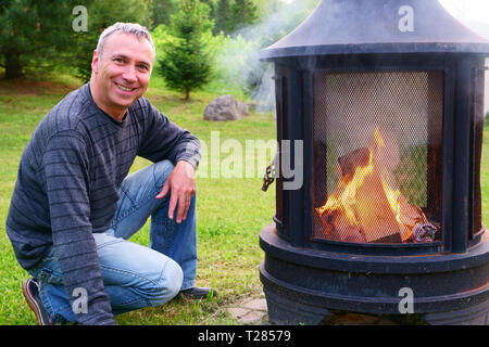 Un homme de race blanche, 50 ans, est sur le point d'allumer sa cheminée en plein air le soir, dans son arrière-cour. Banque D'Images