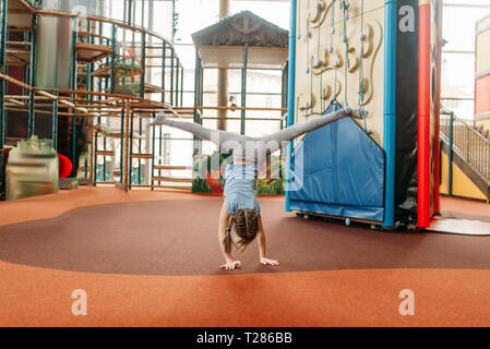 Funny Girl debout sur ses mains à l'envers les enfants dans Game Center. Heureux enfant s'amusant sur l'aire de l'intérieur. Femme enfant jouant dans les Banque D'Images