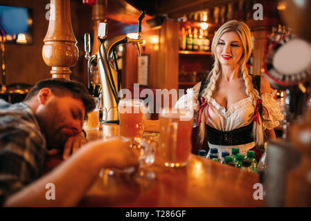 Drunk man sleeping au guichet avec verres en pub, jolie serveuse oktoberfest sur le contexte, les jours fériés. Personne de sexe masculin de l'alcool au bar, la barmaid dans Banque D'Images