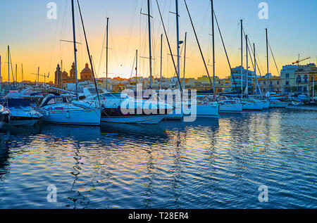 Profitez de la soirée dans le port de Monnickendam avec vue sur les yachts de pompage, de petits bateaux et de l'église paroissiale de St Joseph, cachant le soleil couchant, Malte. Banque D'Images