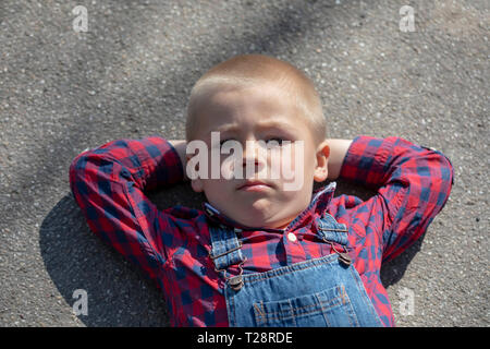 Enfant se trouvant sur le plancher à l'arrière, à la longue. Garçon réfléchi portrait couché sur bras croisés regarder dans la distance Banque D'Images