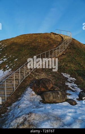 Béton long escalier qui mène au sommet d'une colline entourée par la fonte de la neige sale sur un coucher de soleil de printemps Banque D'Images