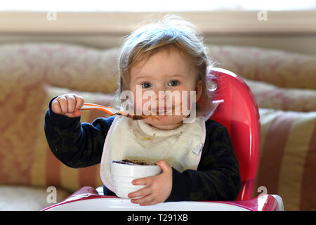 Alimentation bébé fille elle-même avec le chocolat sur son visage Banque D'Images