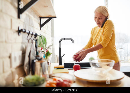 Cheerful woman fruits laver tout en parlant au téléphone Banque D'Images