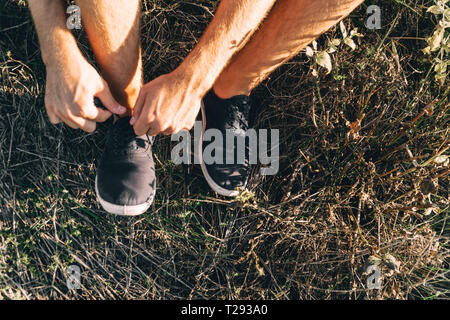 Un homme non identifié sur les lacets des baskets noir assis dans l'herbe du parc se préparent à former Banque D'Images