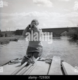 Années 1950, dame agenouillée sur le dos d'un yacht à voile ou bateau à moteur avec un appareil photo prendre une photo, Oxford, Angleterre, Royaume-Uni. Banque D'Images