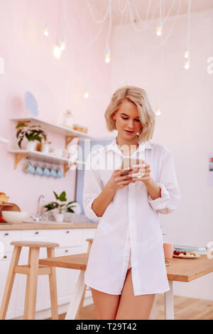 Jeune femme portant une chemise blanche debout dans la cuisine Banque D'Images