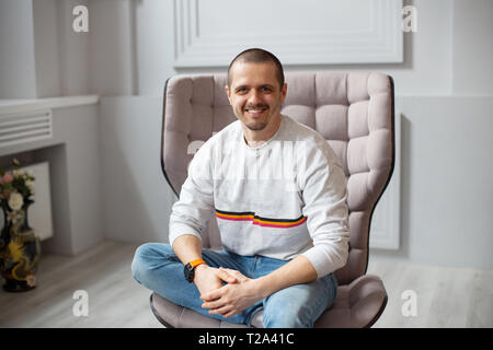 L'homme assis sur une chaise et souriant lookin à huis clos. Portée en jeans Banque D'Images