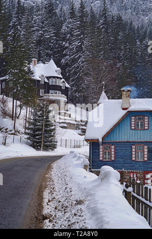 Scène d'hiver dans la région de Red Lake Resort (Roumanie), les maisons couvertes de neige et de forêt près de la route. Banque D'Images