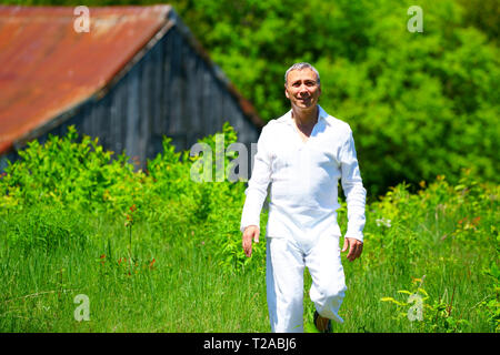 Un homme en habits blancs marcher dans un champ et de toucher les fleurs, entouré de verdure. Banque D'Images