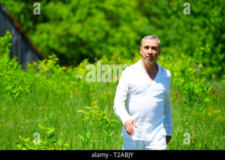 Un homme en habits blancs marcher dans un champ et de toucher les fleurs, entouré de verdure. Banque D'Images