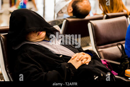 Femme dormir sur une chaise, hood covering face, à l'aéroport de Hong Kong, Hong Kong Banque D'Images