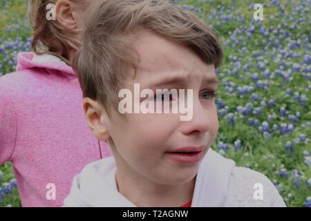 Portrait d'un enfant dans un champ de fleurs sauvages avec une larme couler sur sa joue avec sa soeur apparemment bouleversé Banque D'Images