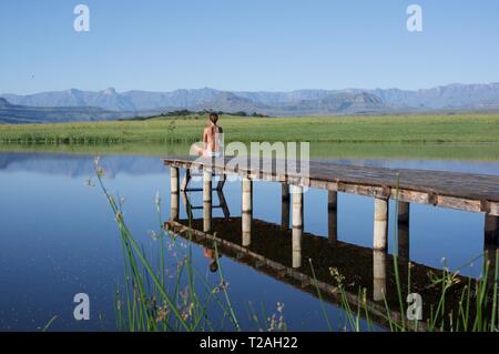Femme assise sur la jetée au bord de l'eau dans les montagnes du Drakensberg Banque D'Images