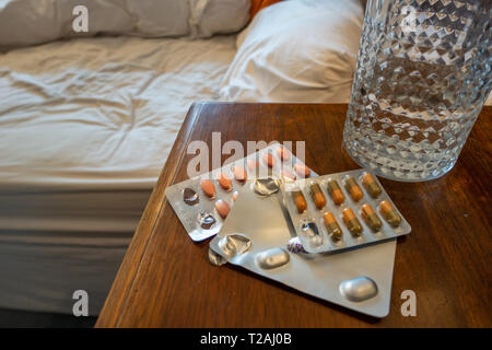 3 paquets de médicaments et un verre d'eau sur une table de chevet Banque D'Images