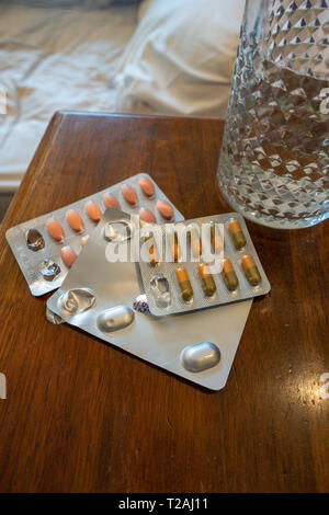 3 paquets de médicaments et un verre d'eau sur une table de chevet Banque D'Images