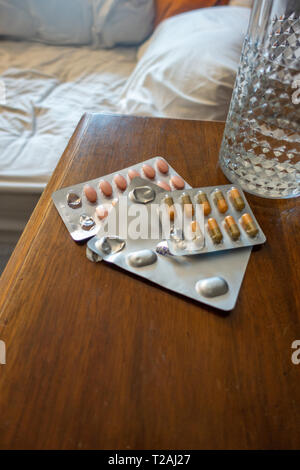 3 paquets de médicaments et un verre d'eau sur une table de chevet Banque D'Images