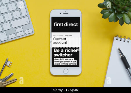 Un iPhone montrant le premier site web direct repose sur un fond jaune table avec un clavier, les touches, le bloc-notes et des plantes (usage éditorial uniquement). Banque D'Images