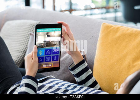 Smart home automation control concpet.woman on sofa using tablet control device dans home.La technologie numérique de vie. Banque D'Images