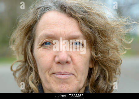 Face aux yeux bleus de la dame d'âge moyen aux cheveux blonds frisés et la peau ridée du point de vue de l'avant en close-up Banque D'Images