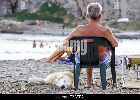 Homme mature reposant sur une chaise à écouter de la musique de flatter son chien sur la plage . Banque D'Images