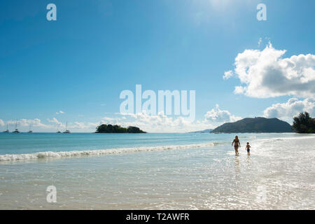 Une mère et son fils marchant dans le surf sur l'Anse Volbert, Praslin, Seychelles Banque D'Images