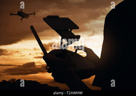 Silhouette vue arrière de l'homme contrôle drone qui vole dans l'air avec arrière-plan de la vue au coucher du soleil Banque D'Images