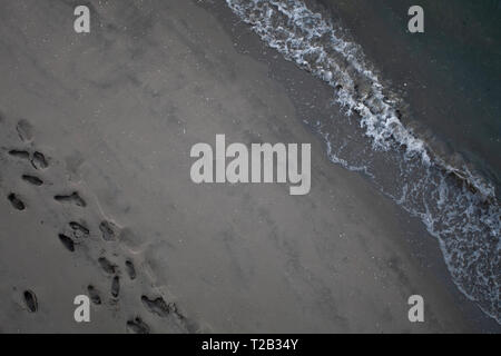 Des traces de pas dans le sable trace un chemin parallèle à l'écraser, les vagues de l'océan le long de la plage du rivage. Banque D'Images