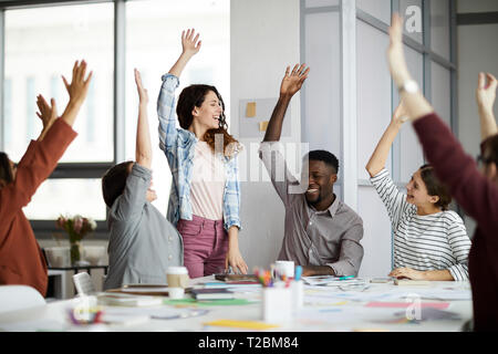 L'équipe multi-ethnique de young businesspeople élever les mains des succès à célébrer dans office, copy space Banque D'Images